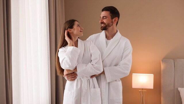 Una pareja en batas blancas, en una habitación de hotel.