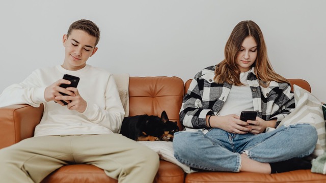 Pareja joven distanciada cada uno viendo sus celulares.
